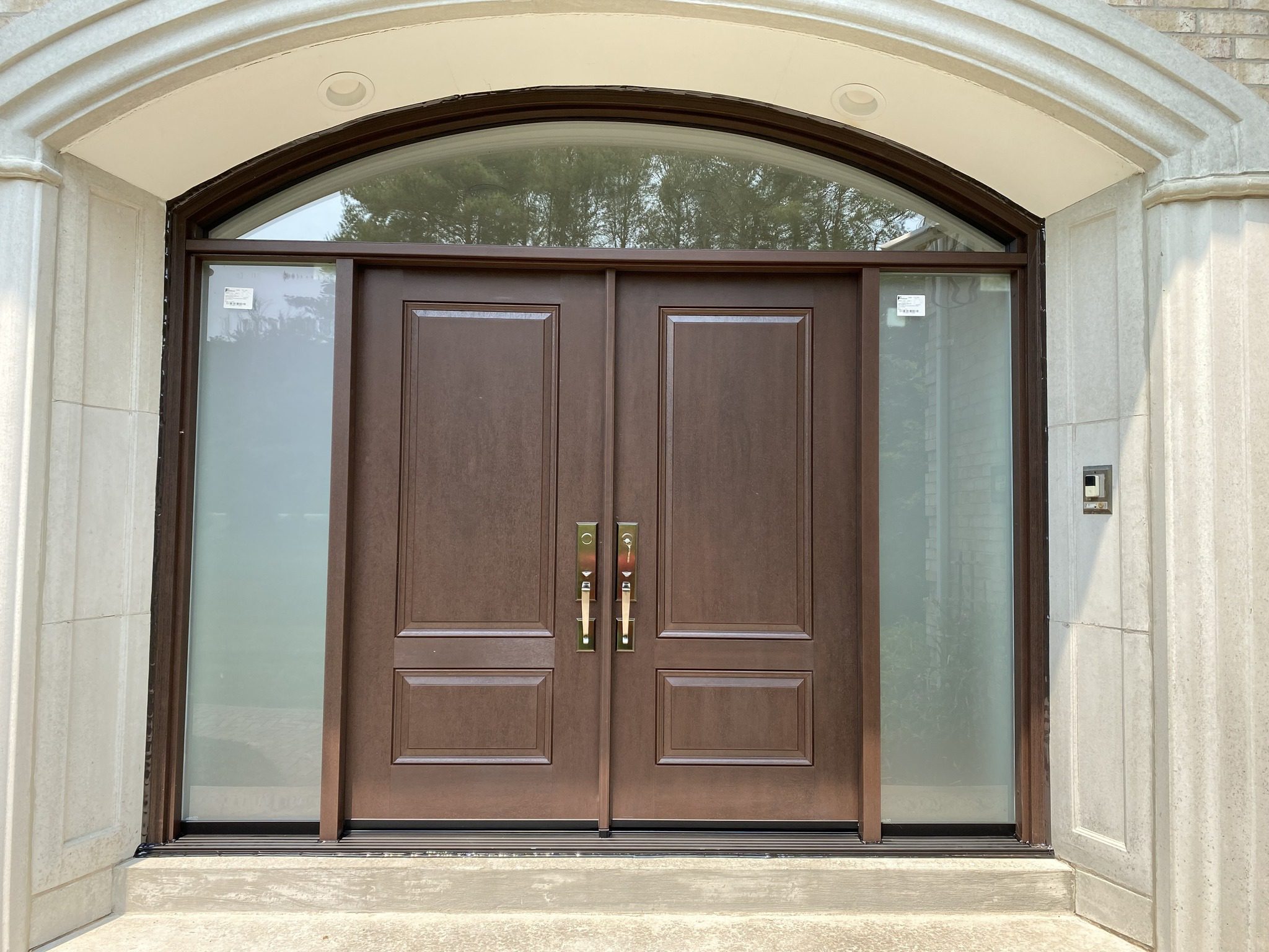 Double entry door installation with arched transom in a stone home exterior