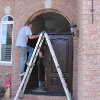 Front door installation in progress on an arched entry using ladder at a residential home